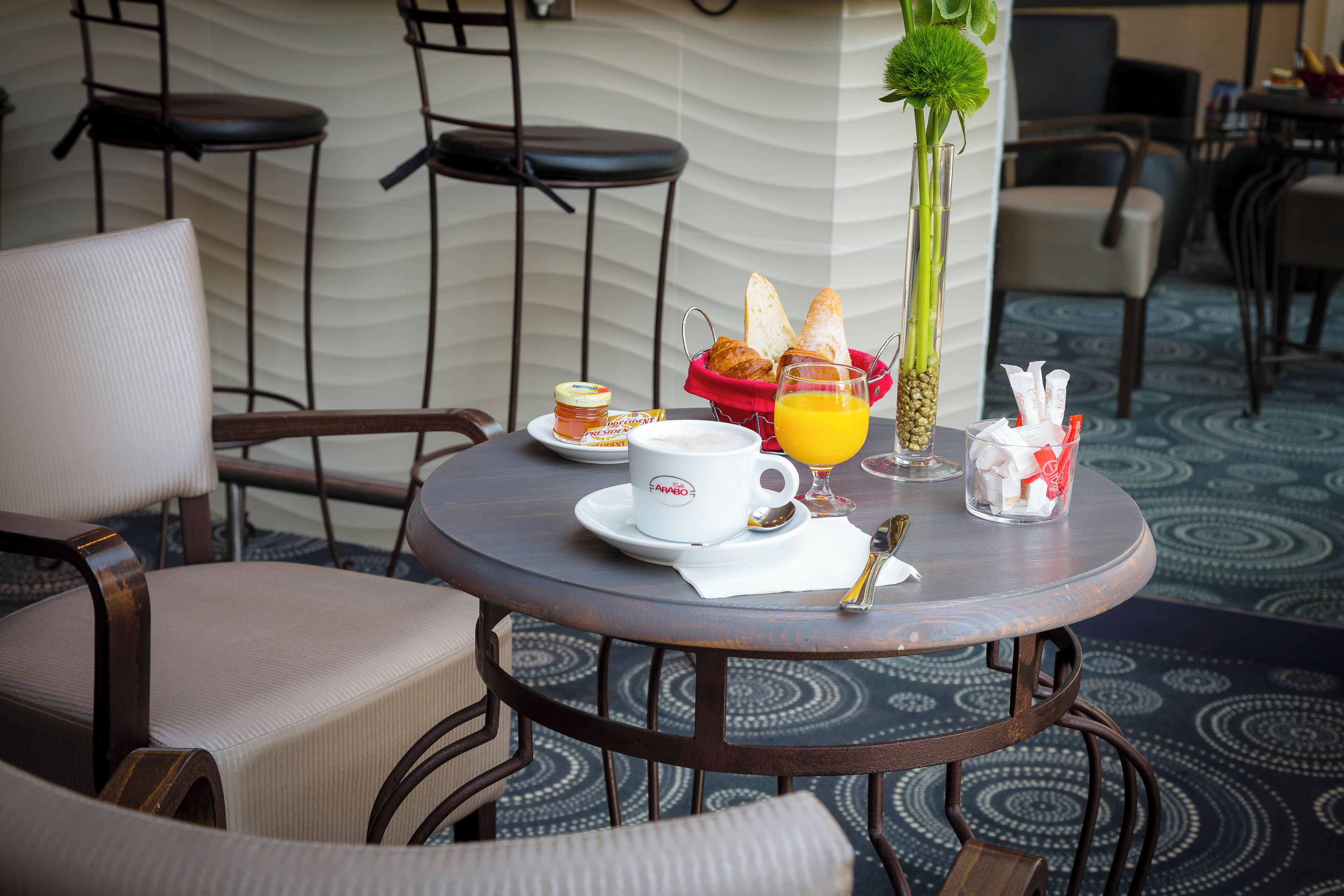 A round table with breakfast items, a vase with a flower, and a chair with a cushion.