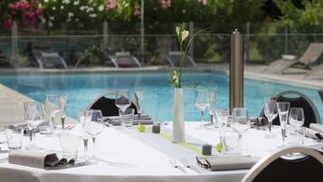 Mesa preparada para comer con vista a una piscina y sillones de descanso al fondo.