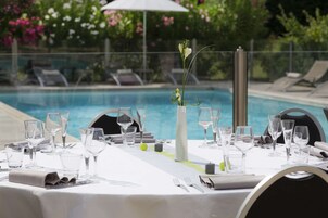 Mesa preparada para comer con vista a una piscina y sillones de descanso al fondo.