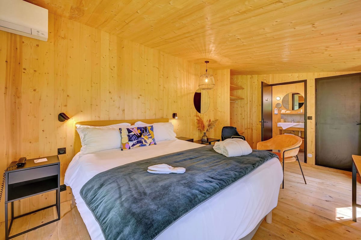 A wooden-paneled bedroom with a bed, bedside table, chair, and a mirror.