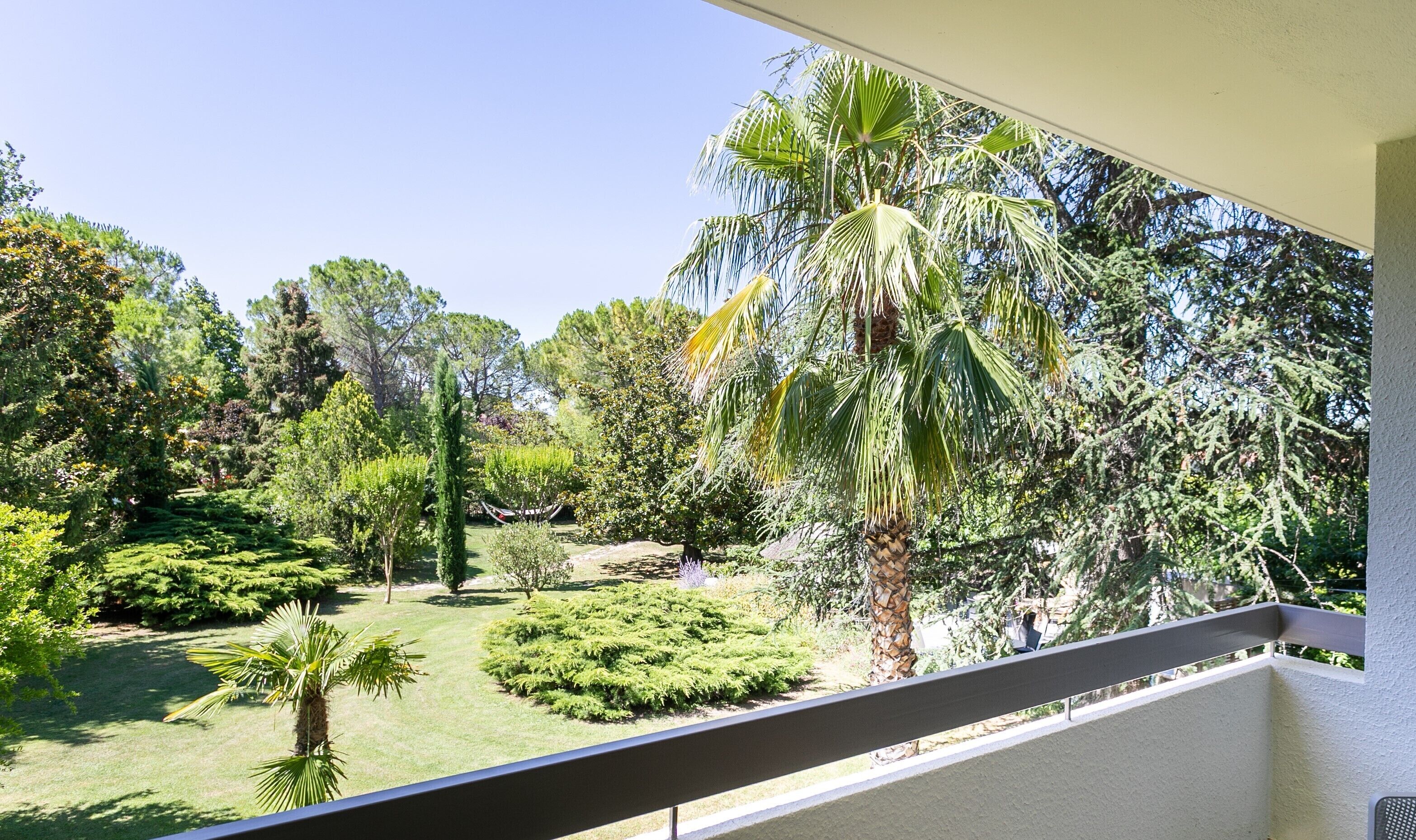 A balcony with a view of a well-maintained garden featuring various trees and shrubs.