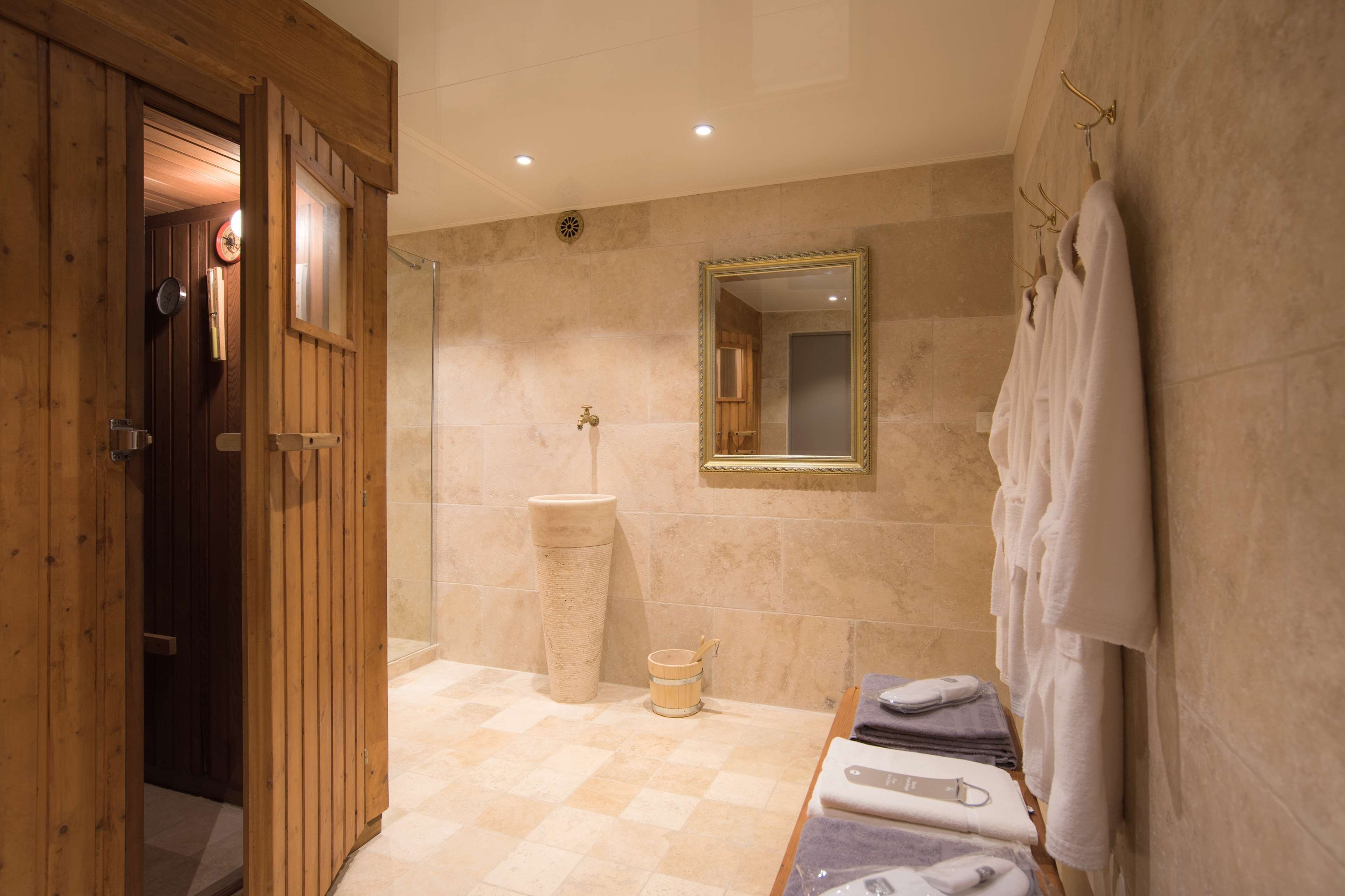 Ein Badezimmer mit Holztür, Waschbecken, Spiegel und Handtüchern an einem Ablagegestell.
