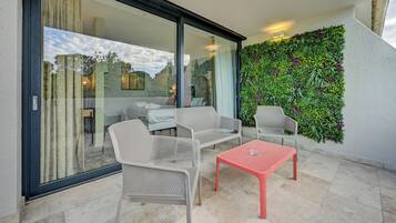 A balcony with wicker furniture, a red table, and a green vertical garden.