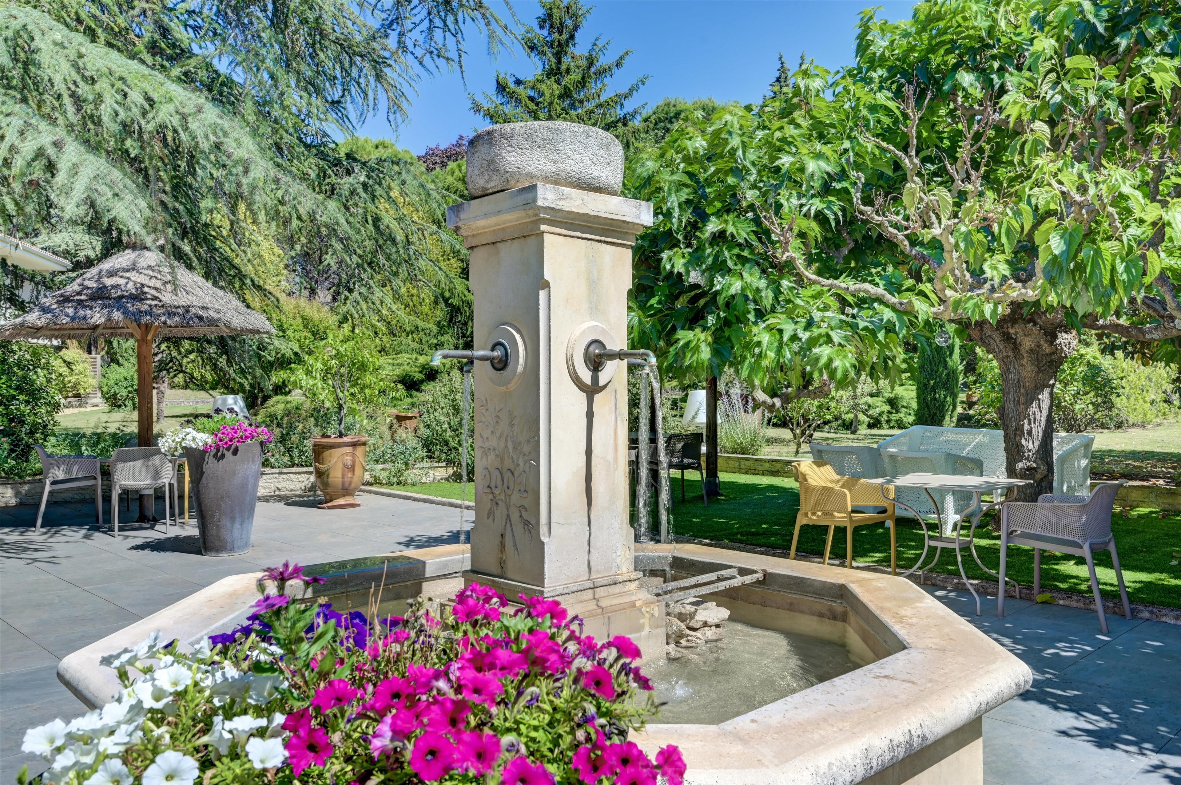 A garden with a fountain, outdoor seating, and a stone structure.