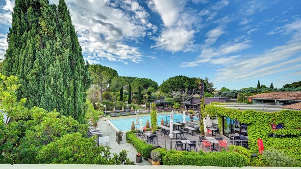 A rooftop pool area with outdoor seating, surrounded by lush greenery and tall trees. - Best Western Sevan Parc Hotel (Pertuis)