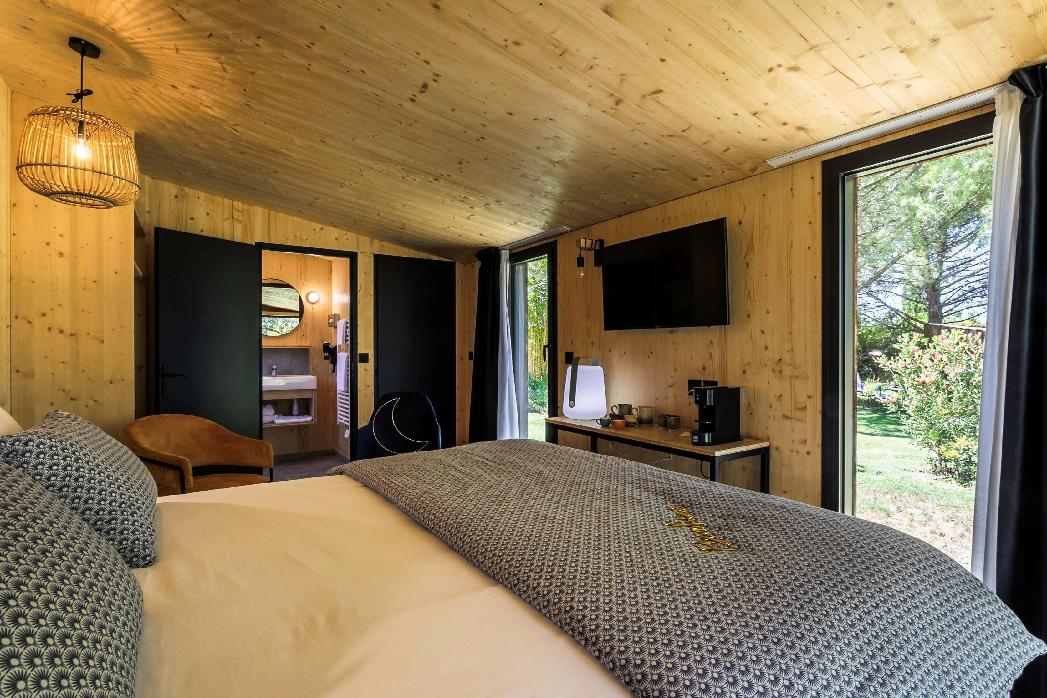 Een kamer met houten lambrisering, een bed, een bureau, een stoel, een televisie en een raam.