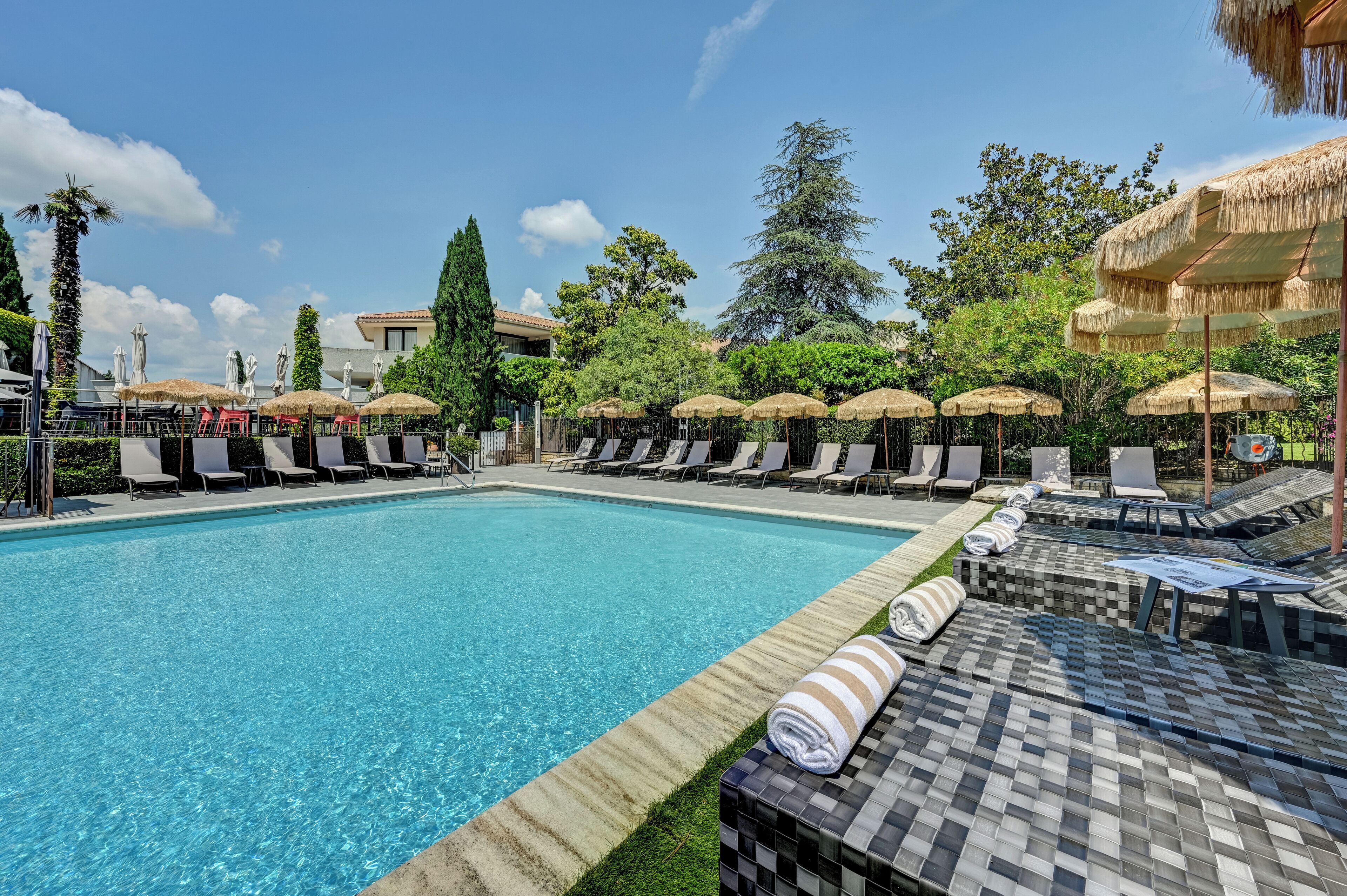 Une piscine entourée de verdure et d’arbres, avec des chaises longues et des parasols.