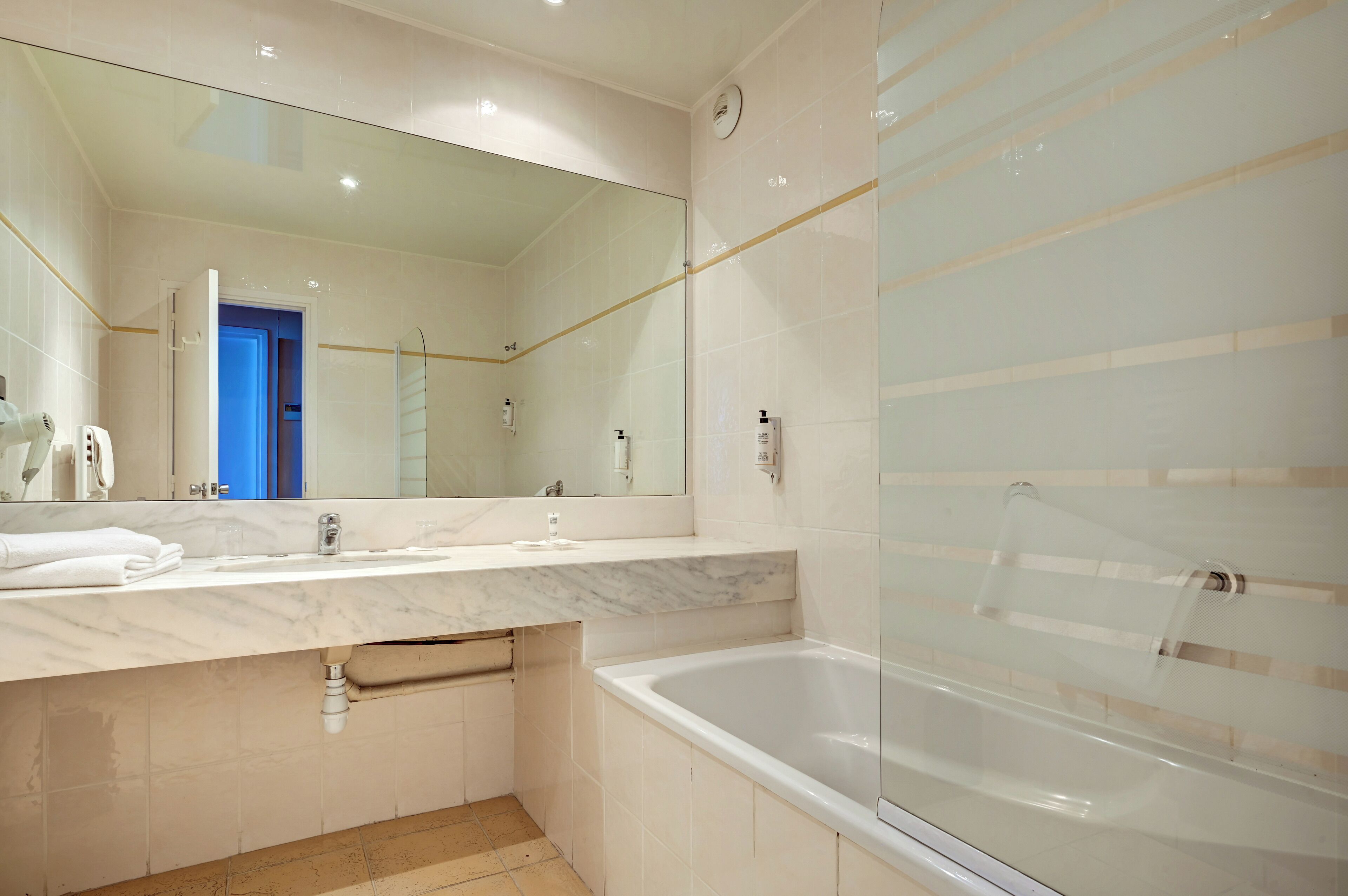 Ein modernes Badezimmer mit einem großen Spiegel, einer Badewanne und einem Waschtisch mit Marmorplatte.