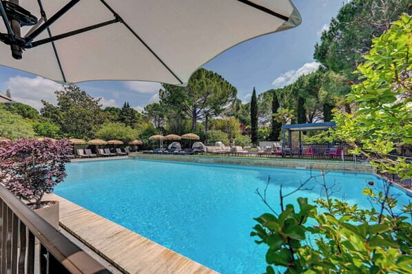 Una piscina al aire libre, sombrillas, sillones reclinables de piscina