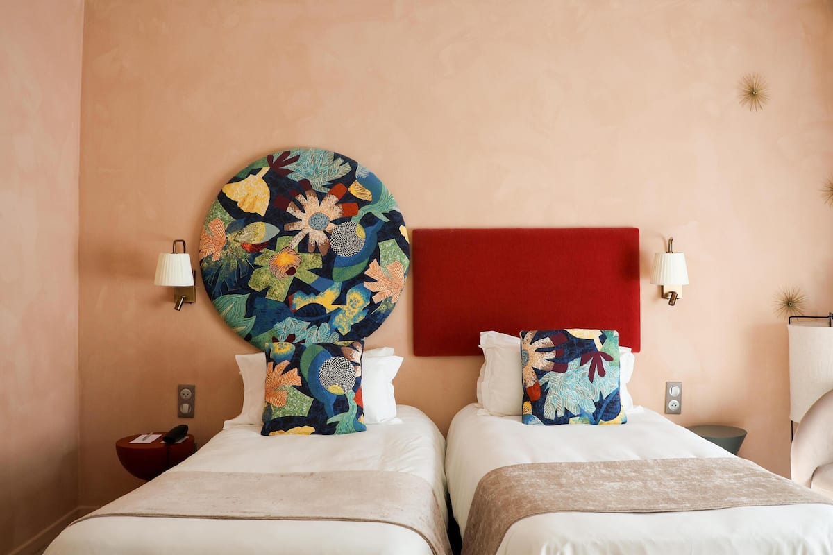 A hotel room with two beds, a red accent wall, and a large floral artwork above the beds.