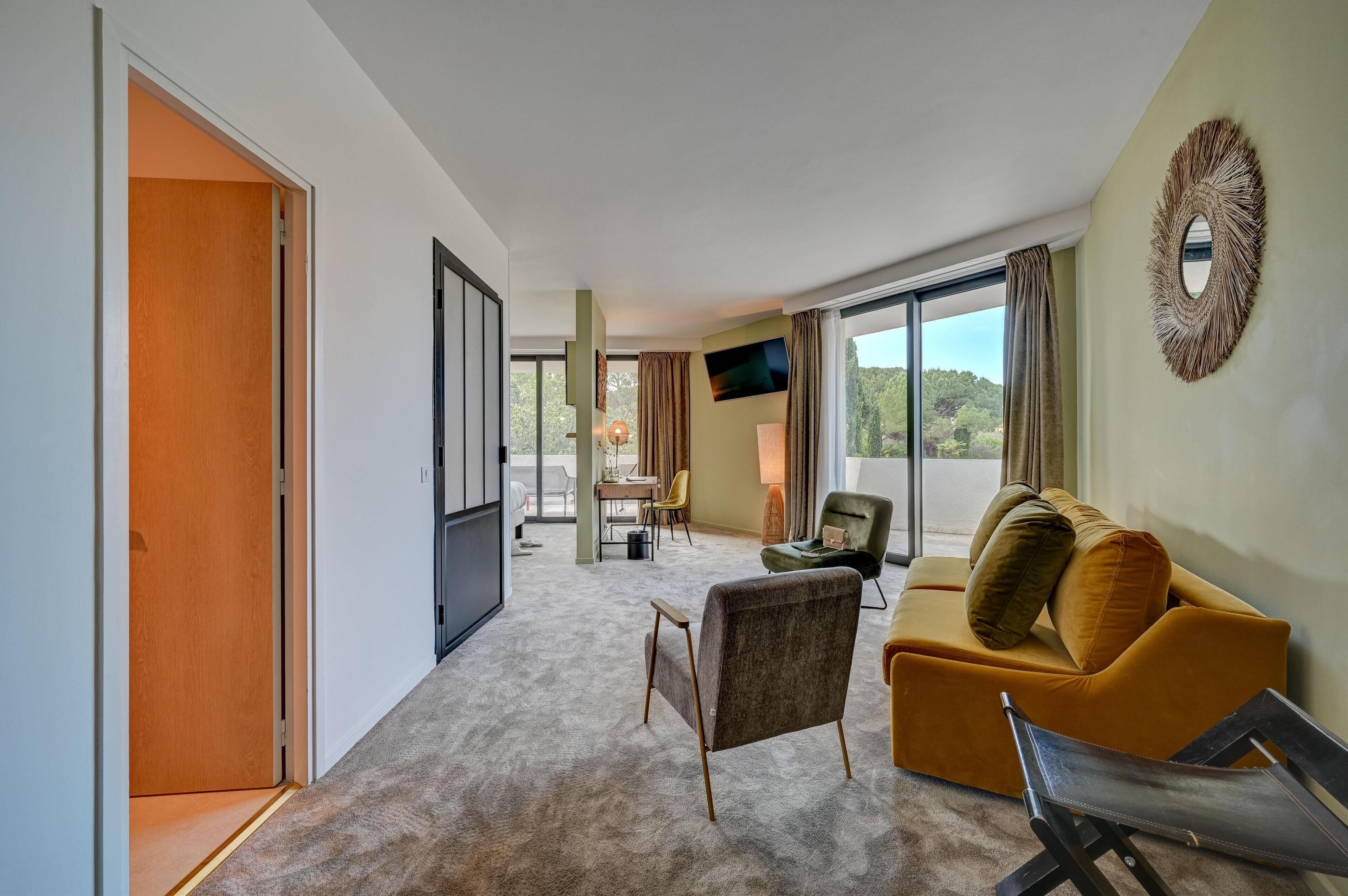 Una habitación de hotel moderna con sofá, sillón y zona de comedor con mesa y sillas.