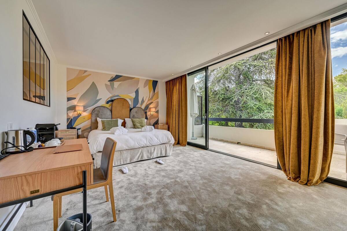 A hotel room with a bed, a desk, a chair, a coffee maker, and a view of the outdoors.
