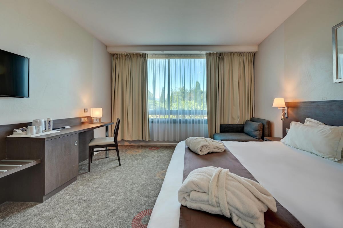 A hotel room with a bed, a desk, a chair, a TV, and a window with curtains.