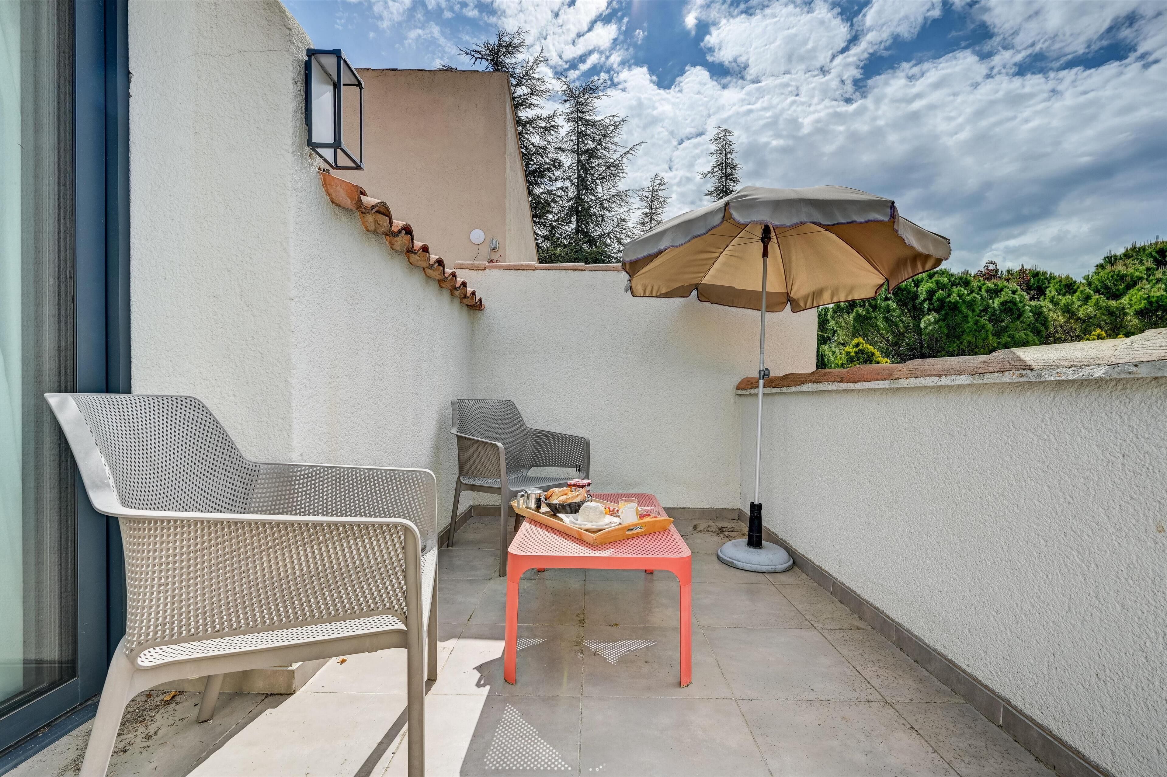 Ein Balkon mit einem weißen Stuhl, einem Tisch mit einer Auflage und einem beige gefärbten Sonnenschirm.