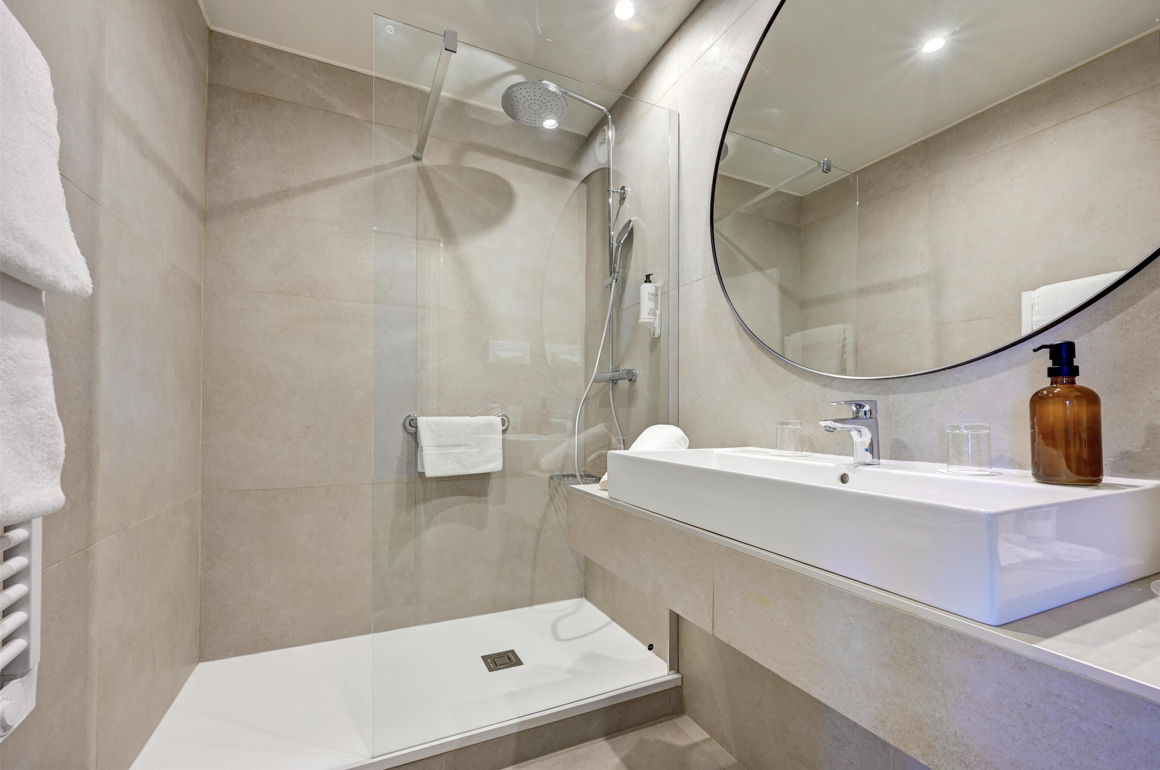 Un baño moderno con ducha acristalada, lavamanos blanco y un espejo grande.