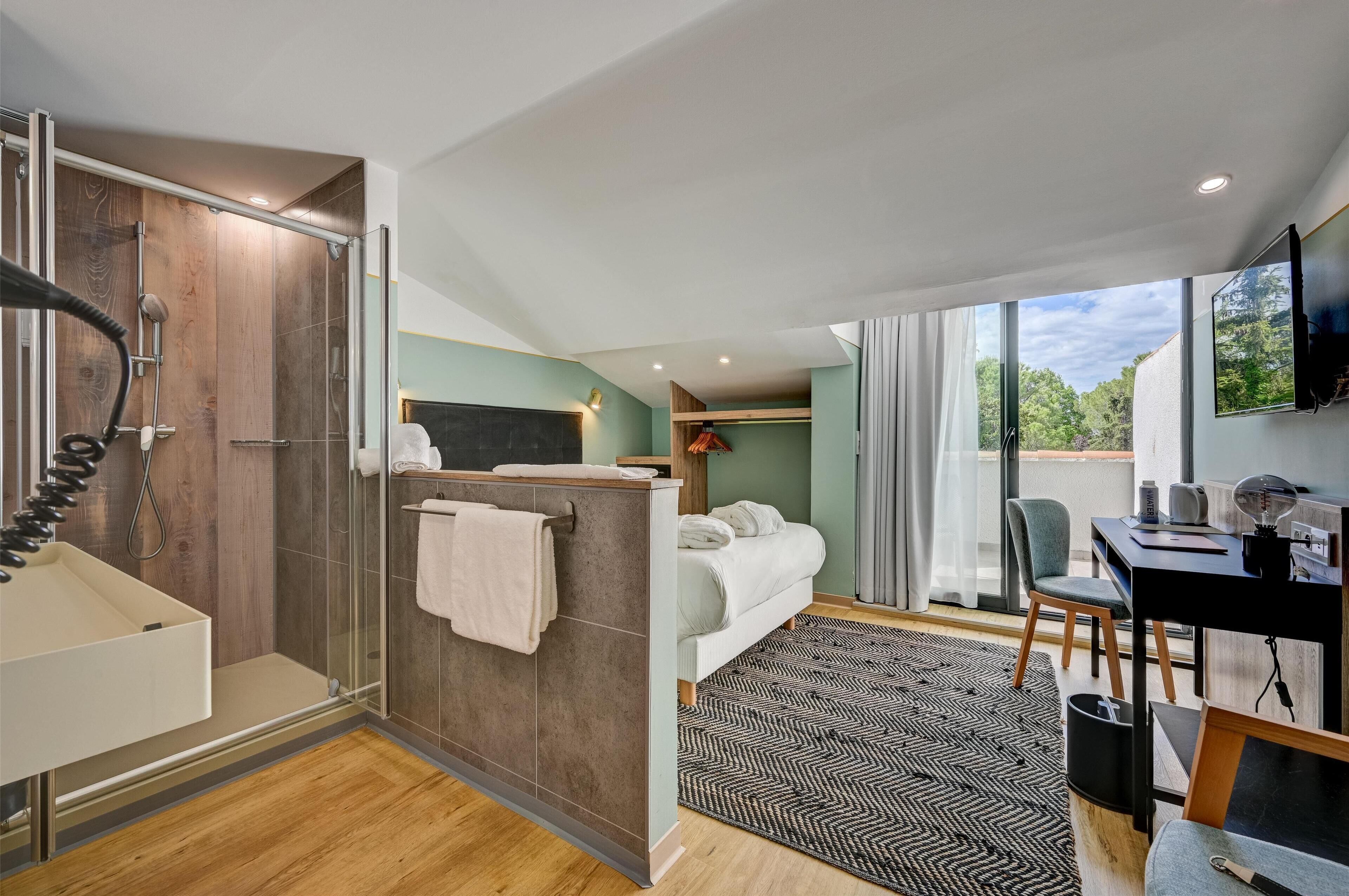 A modern hotel room with a shower, a bed, a desk, and a large window offering a view of the outdoors.