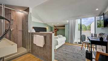 A modern hotel room with a shower, a bed, a desk, and a large window offering a view of the outdoors.