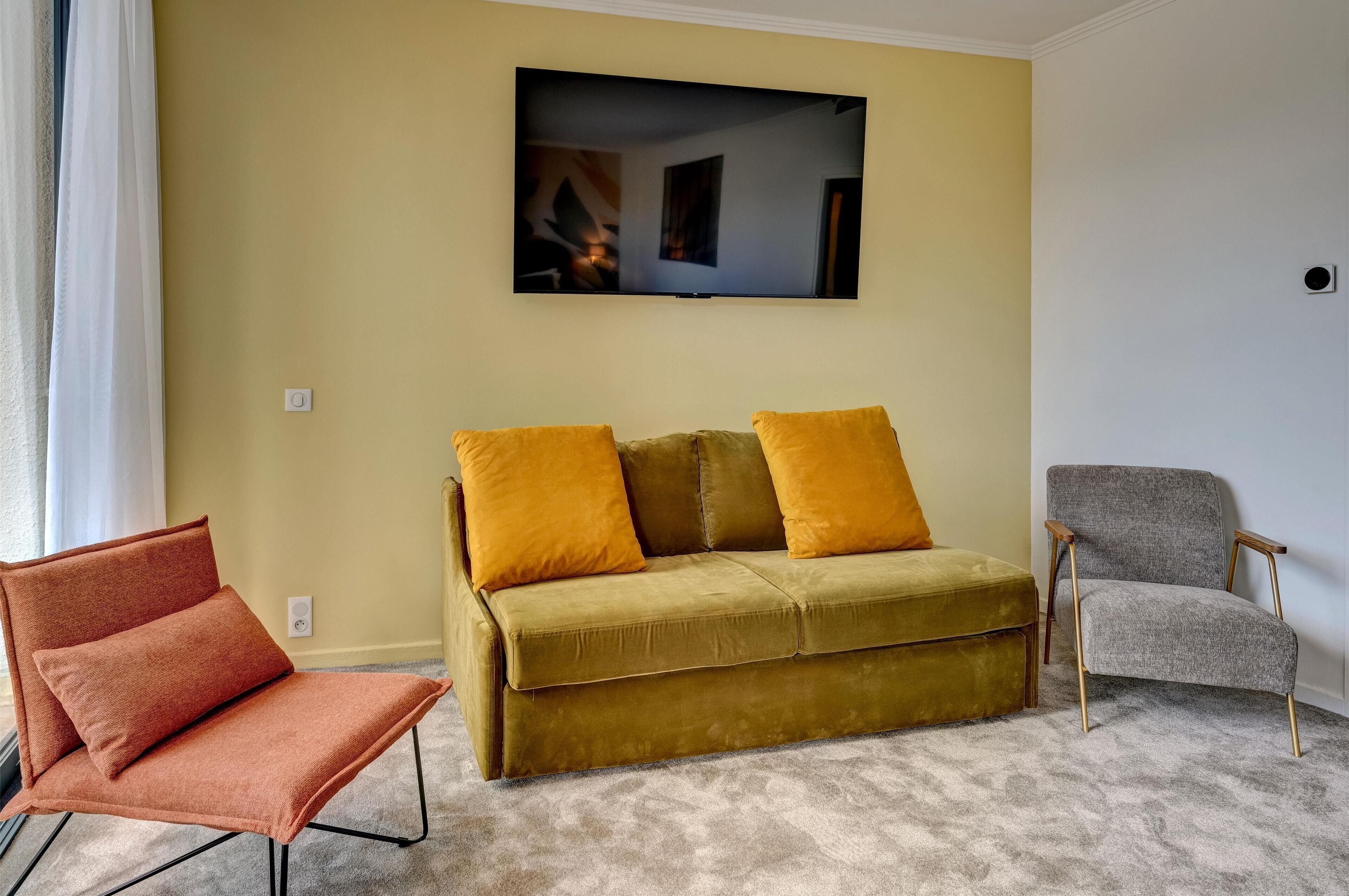 A living room with a sofa, two armchairs, and a flat-screen TV on the wall.