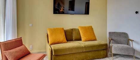 A living room with a sofa, two armchairs, and a flat-screen TV on the wall.