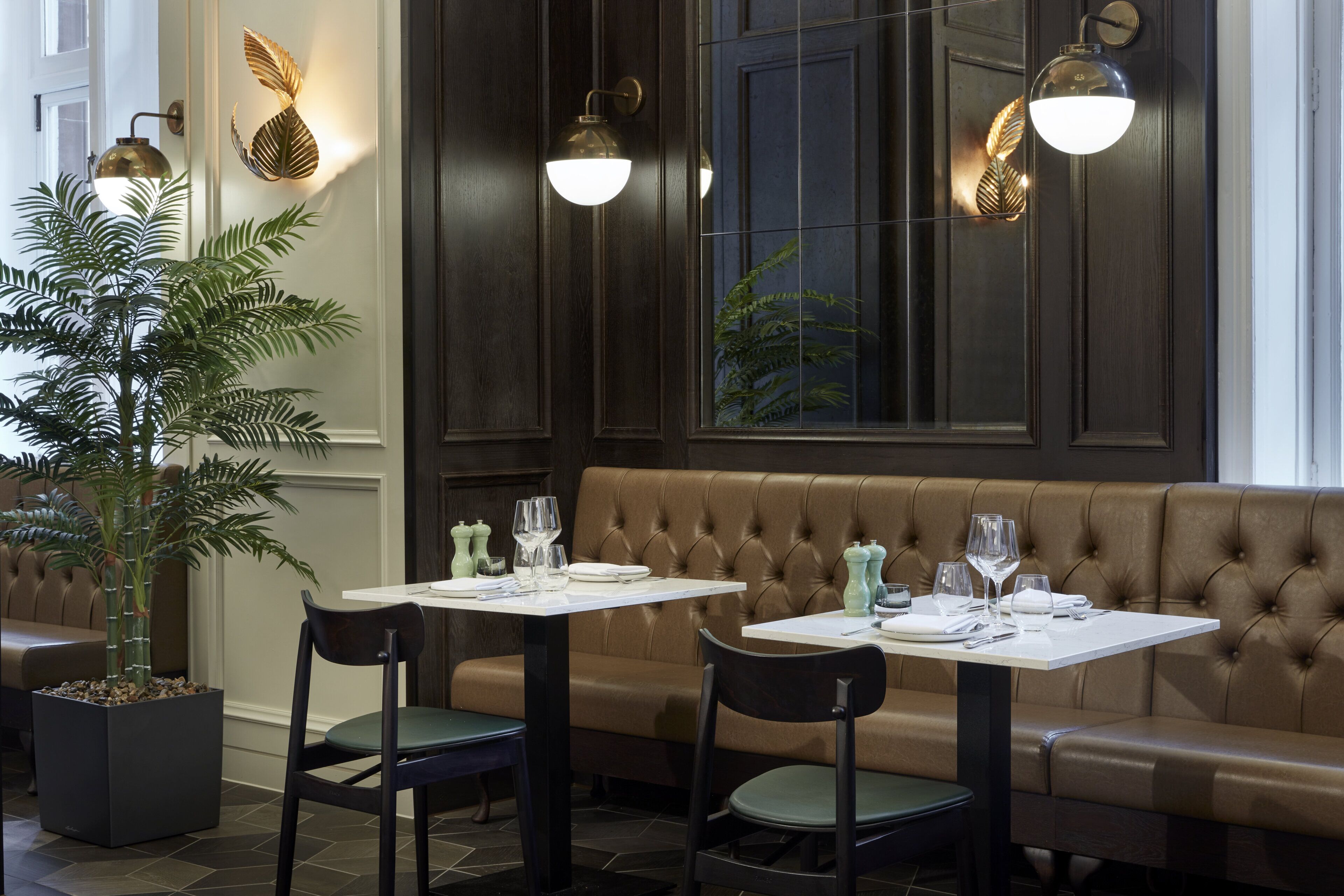 Un restaurante con pared de madera oscura, una banqueta de cuero con capitoné y dos mesas con sillas.