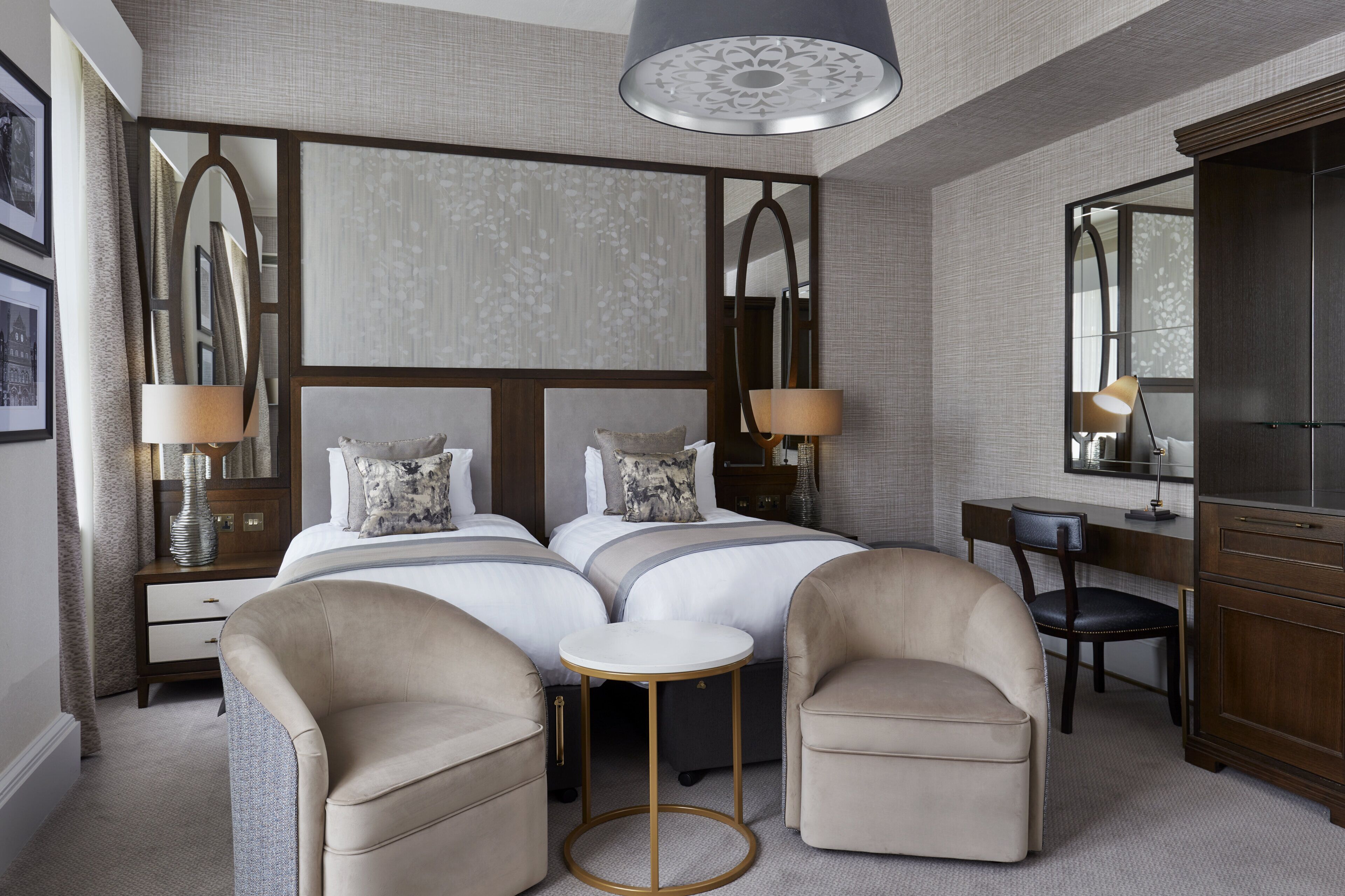 A hotel room with two beds, a desk, a chair, a small table, and a wardrobe.