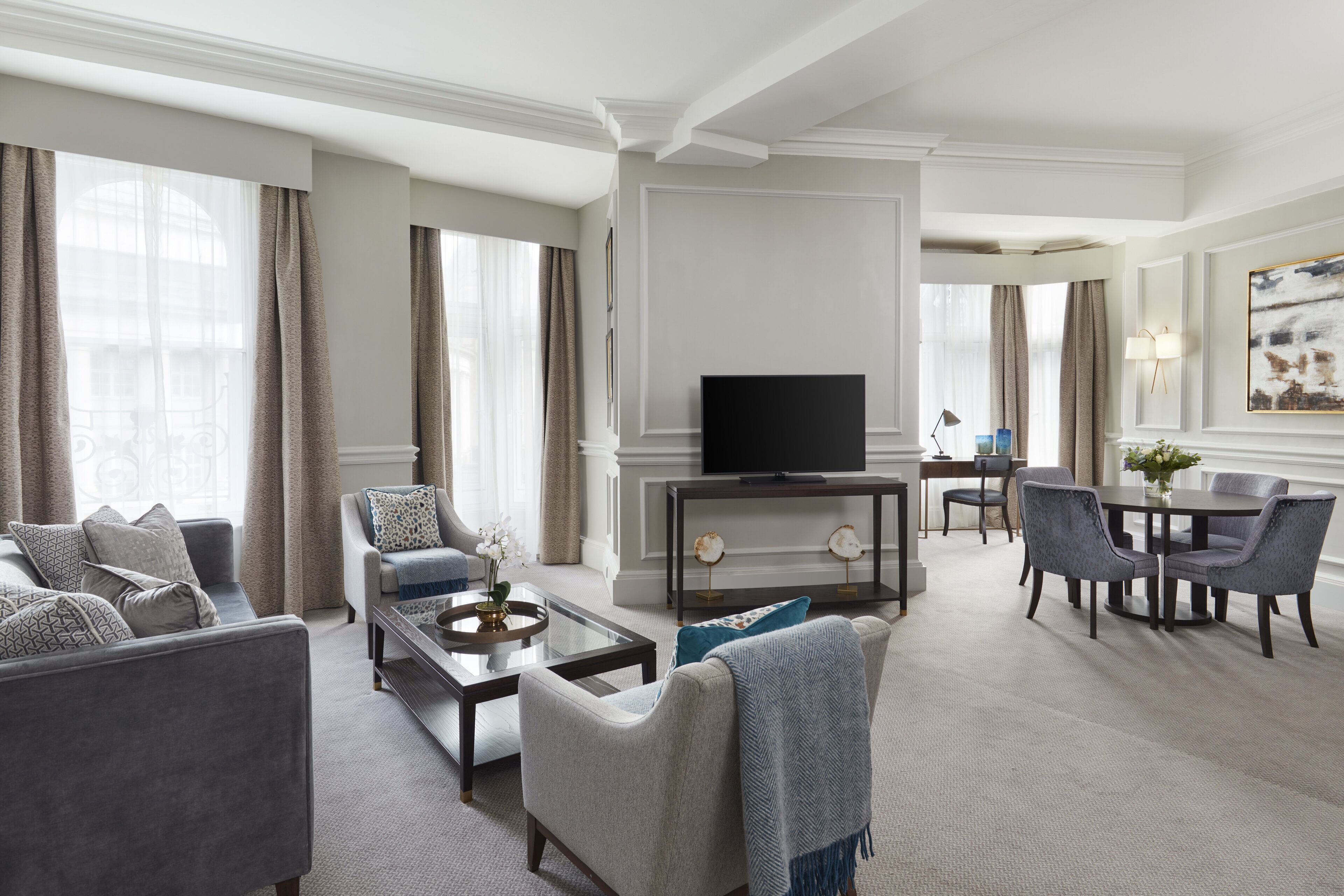 A modern living room with a flat-screen TV, comfortable seating, a dining area, and a large window with curtains.