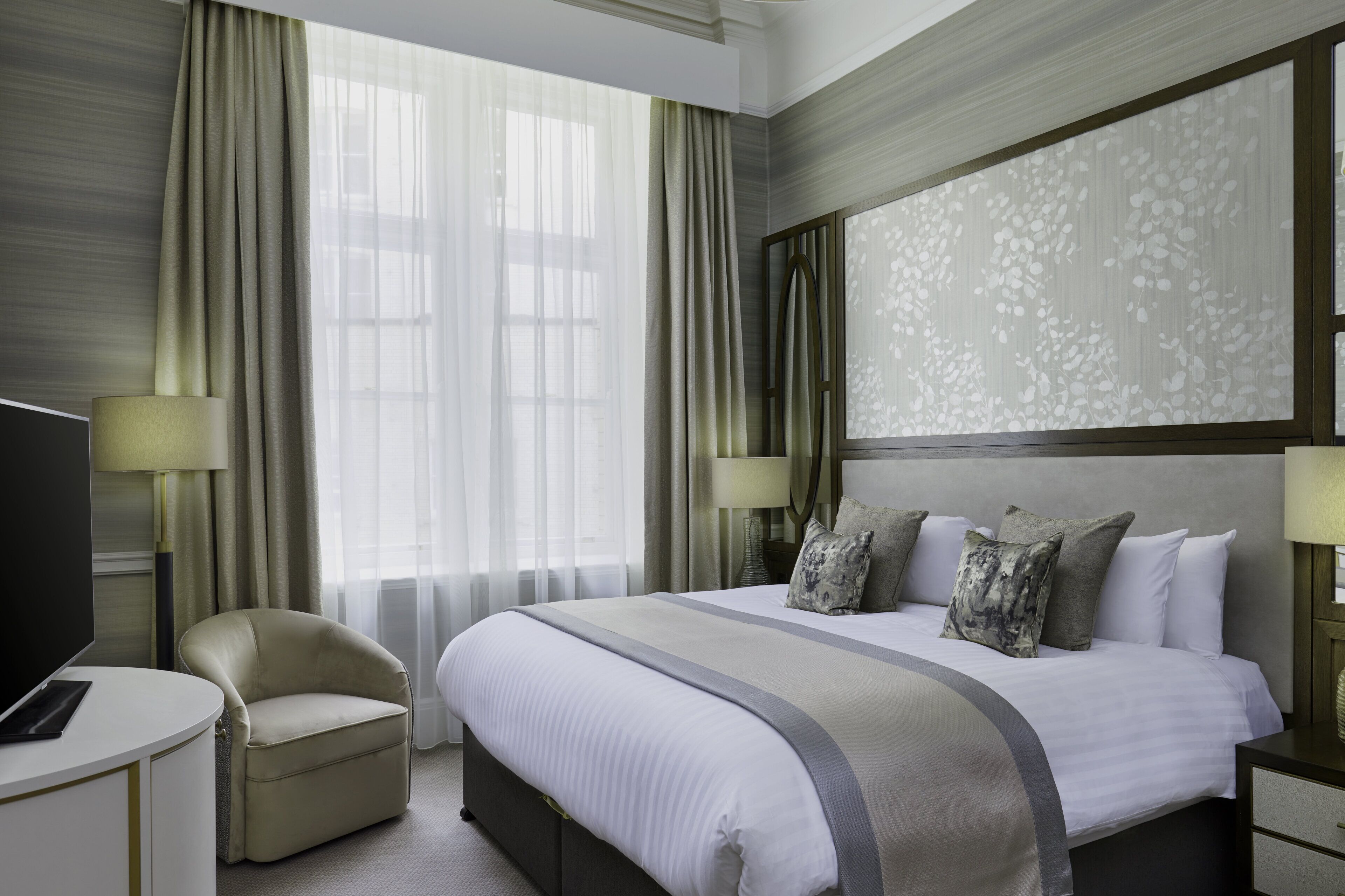 A hotel room with a large bed, a chair, a TV, and a desk.
