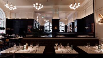 A restaurant with marble tables, dark booths, and chandeliers.