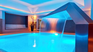 A modern indoor pool with a waterfall feature, surrounded by a minimalist design and ambient lighting.