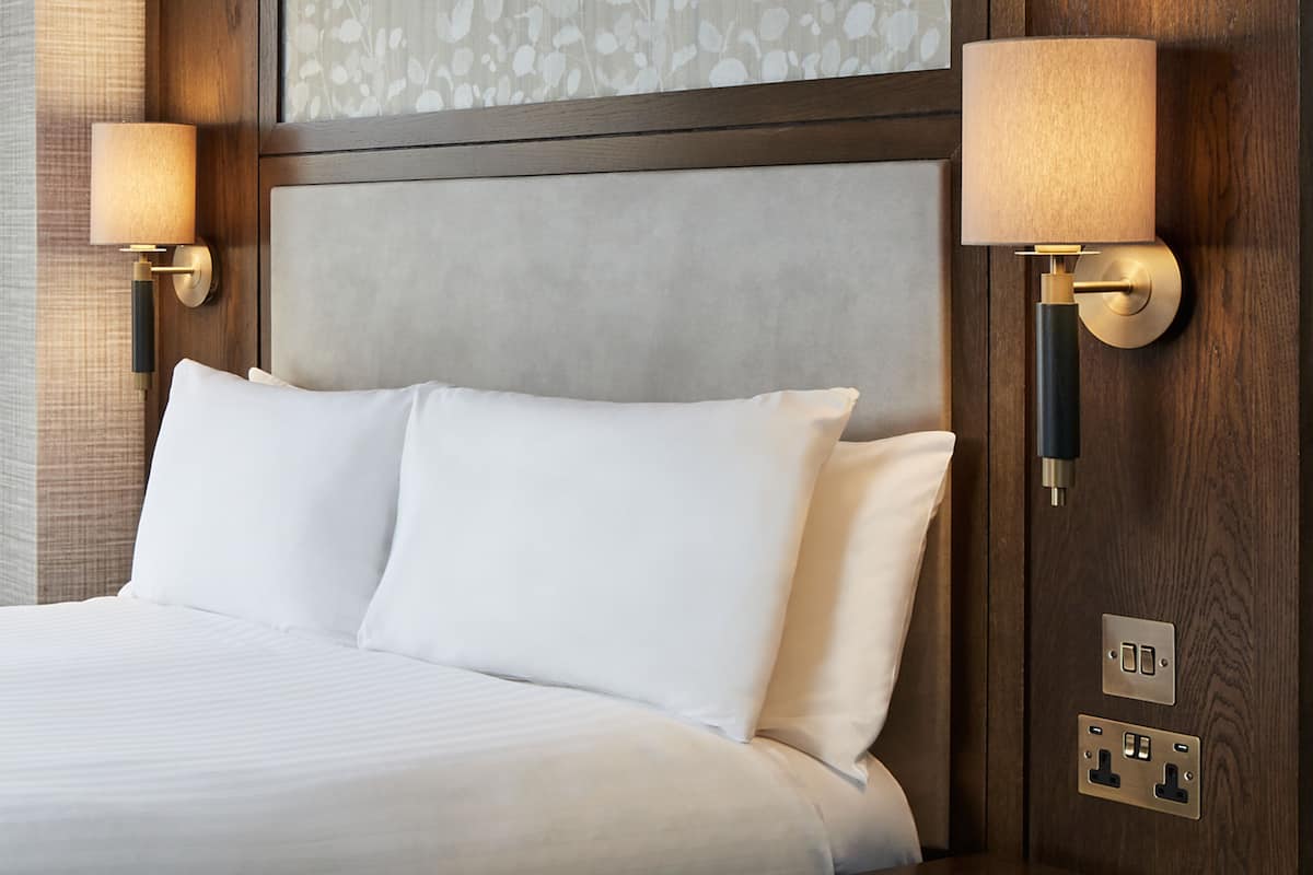 A hotel room with a large bed, two wall-mounted lamps, and a wooden headboard.