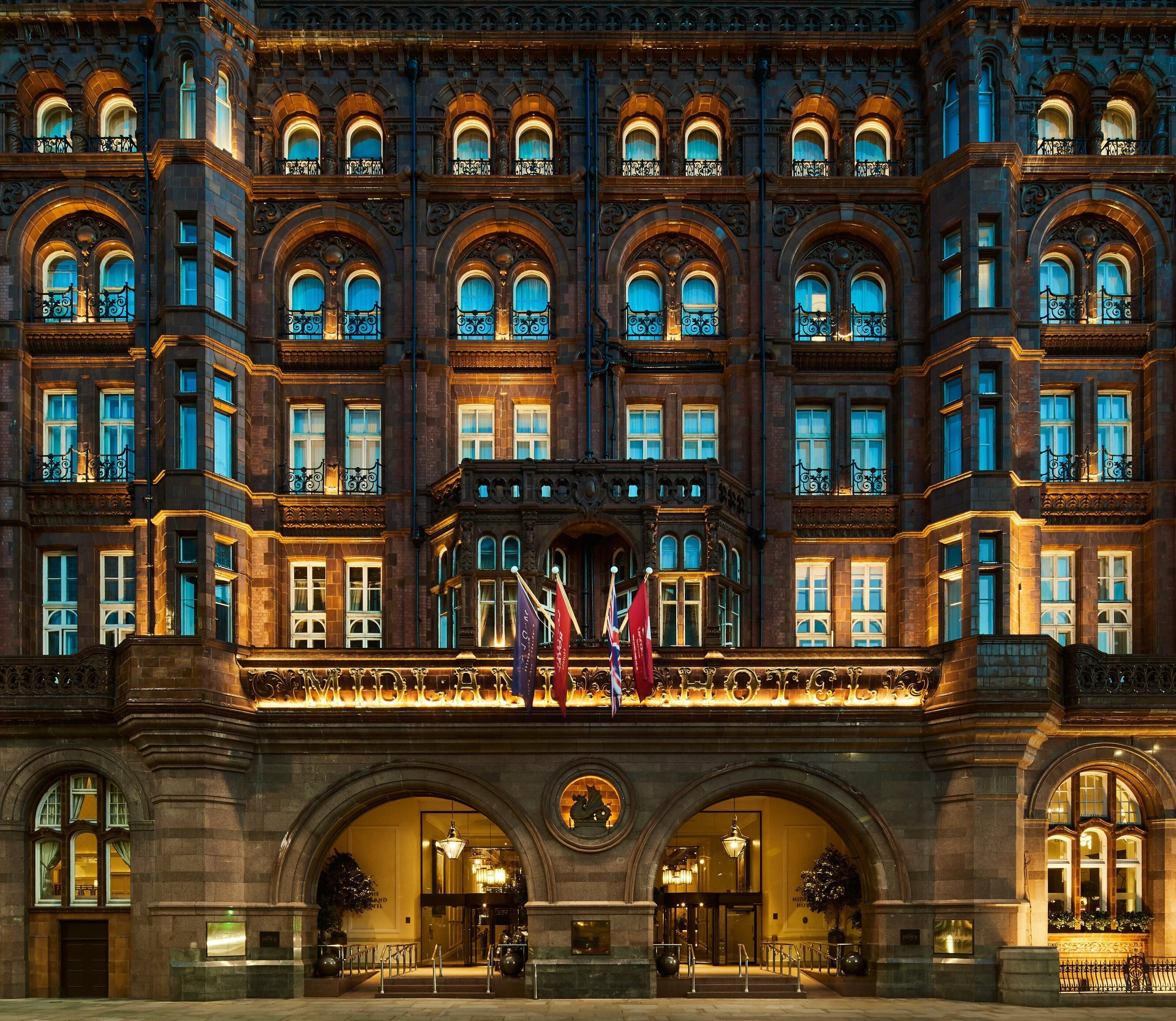 A grand hotel facade with multiple arched windows, a central entrance with a canopy, and flags.