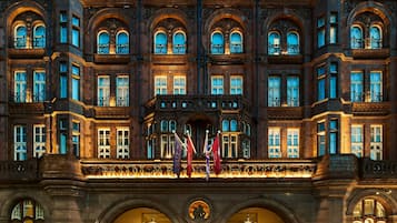 A grand hotel facade with multiple arched windows, a central entrance with a canopy, and flags.