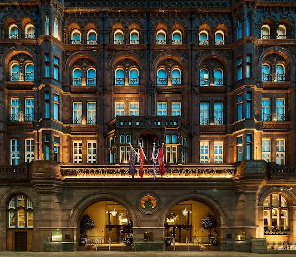 A grand hotel facade with multiple arched windows, a central entrance with a canopy, and flags.