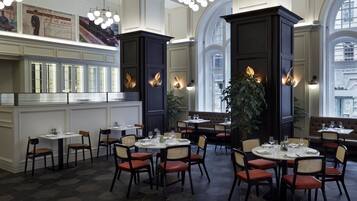 Un restaurante con techos altos, amplias ventanas y diferentes opciones de asientos, incluyendo mesas y cabinas.
