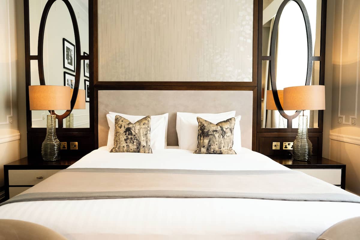A hotel room with a large bed, two bedside lamps, and a mirror above the bed.