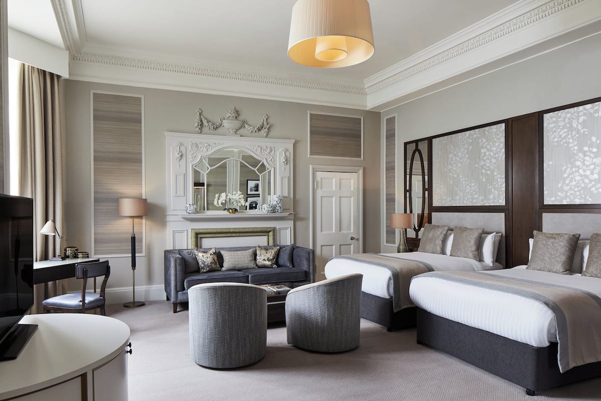 A hotel room with a large bed, a sofa, two armchairs, a desk, and a television.