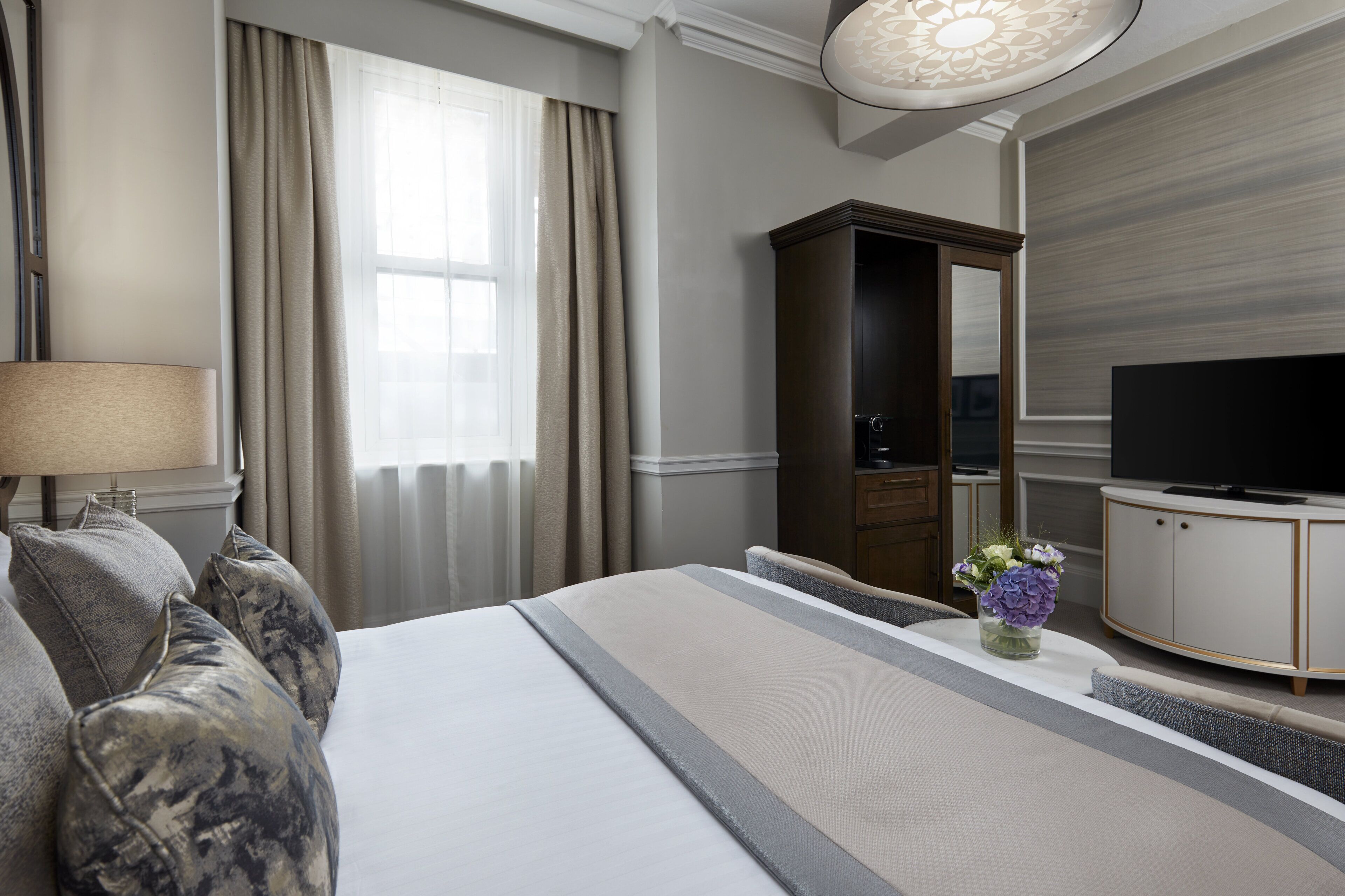 A hotel room with a bed, a television, a dresser, and a vase of flowers.