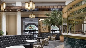 A modern lobby with a curved bar, leather seating, wicker chairs, and a large tree.