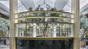 Zona de bar circular con copas y botellas, rodeada de columnas de mármol y un techo de cristal con plantas.