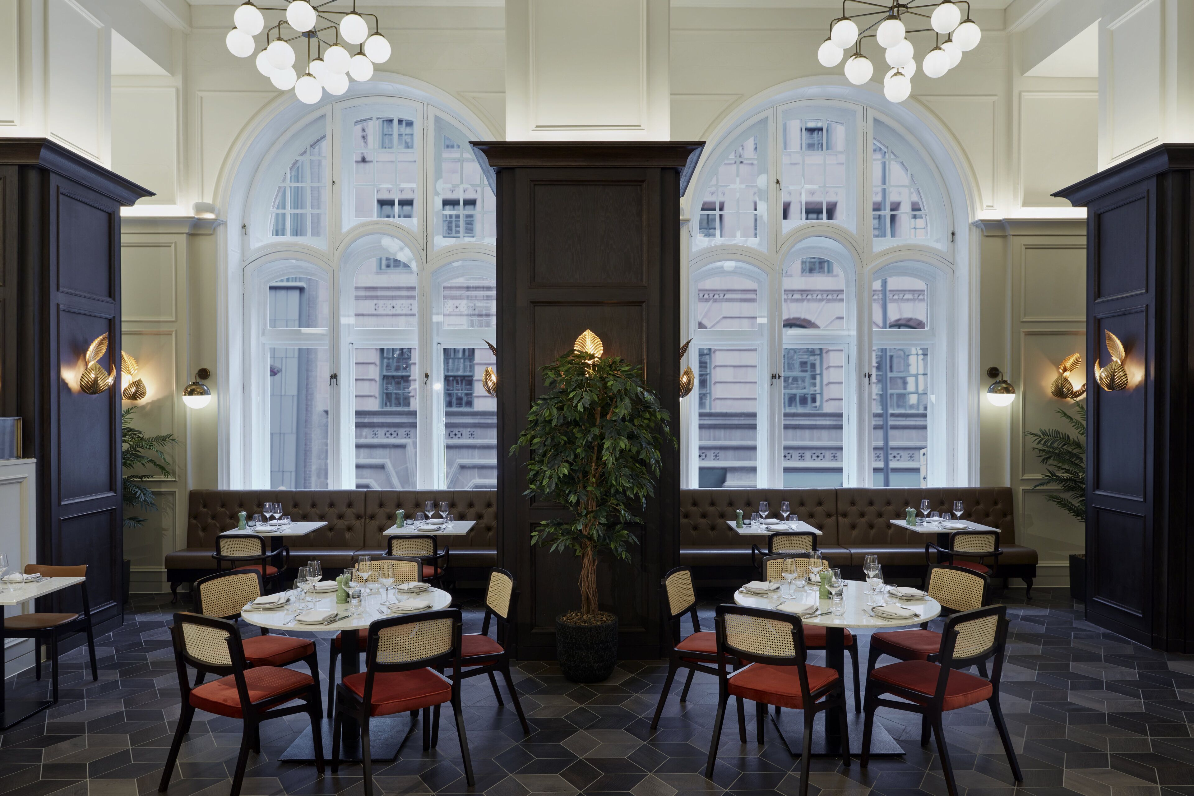 Un restaurant doté de grandes fenêtres en arc, d’une plante centrale et de plusieurs espaces aménagés pour s’asseoir.