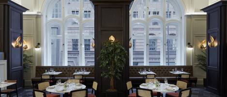 Un restaurant doté de grandes fenêtres en arc, d’une plante centrale et de plusieurs espaces aménagés pour s’asseoir.