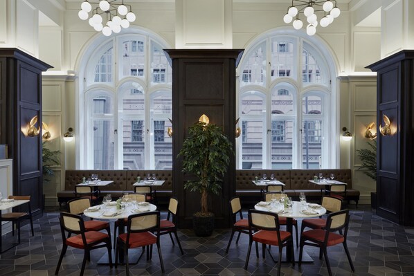 Un restaurant doté de grandes fenêtres en arc, d’une plante centrale et de plusieurs espaces aménagés pour s’asseoir.