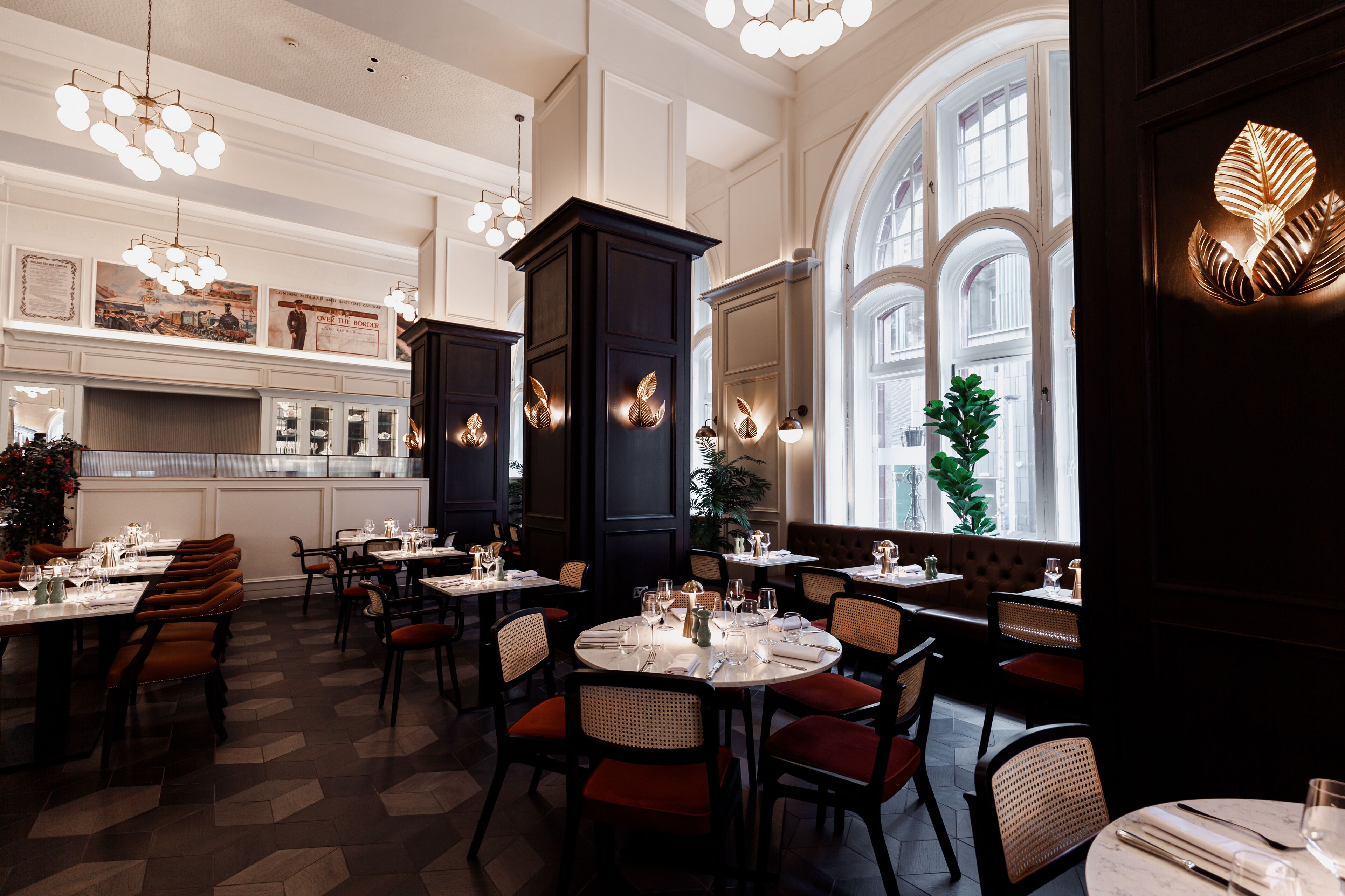 A restaurant with round tables, dark wooden pillars, and a large arched window.