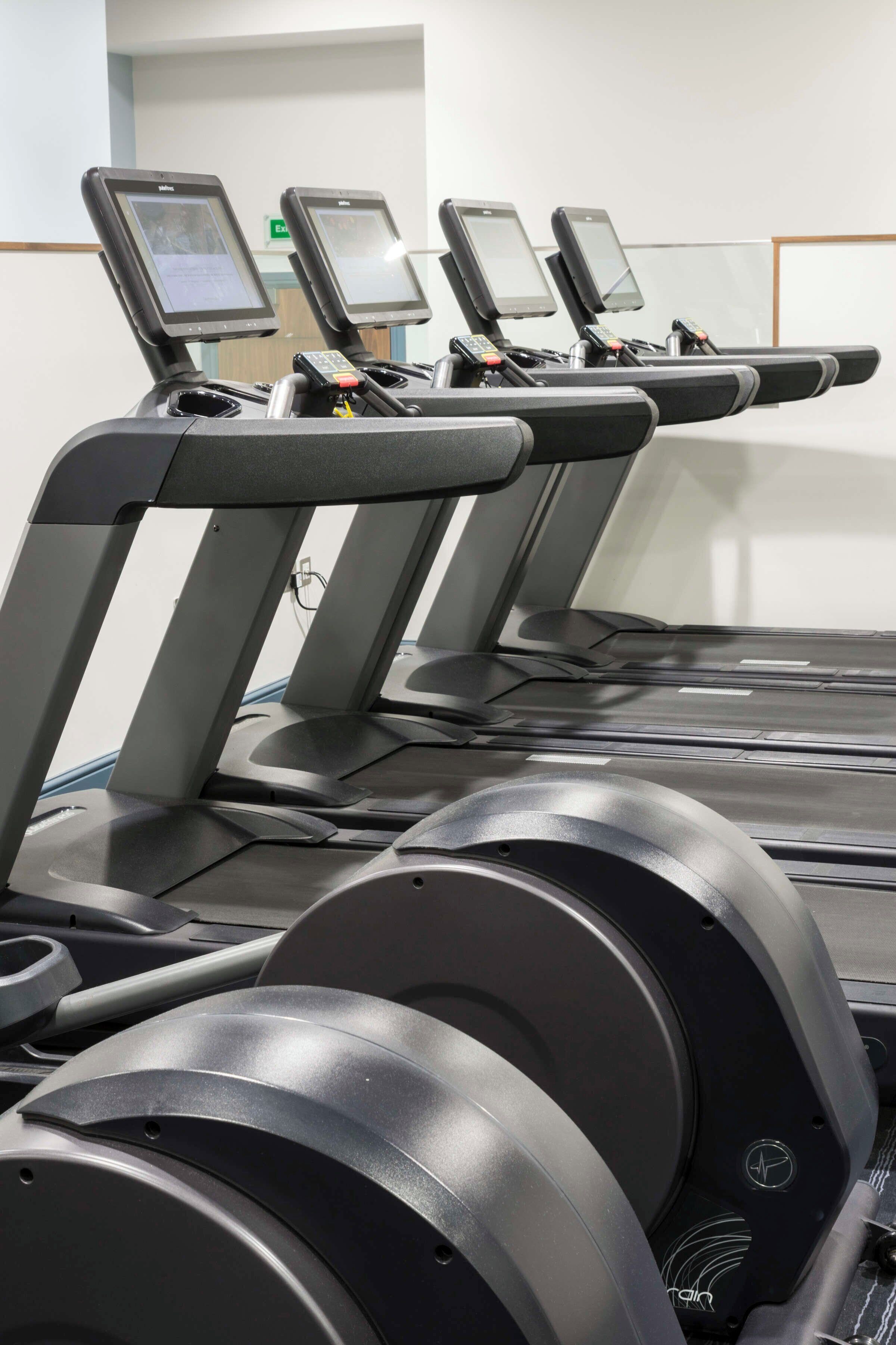 A row of treadmills with digital screens, a control panel, and a water bottle holder.