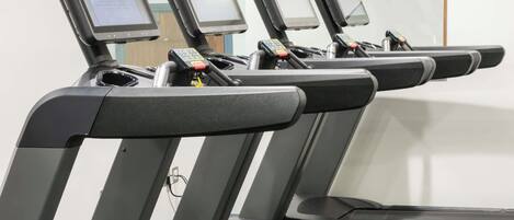 A row of treadmills with digital screens, a control panel, and a water bottle holder.