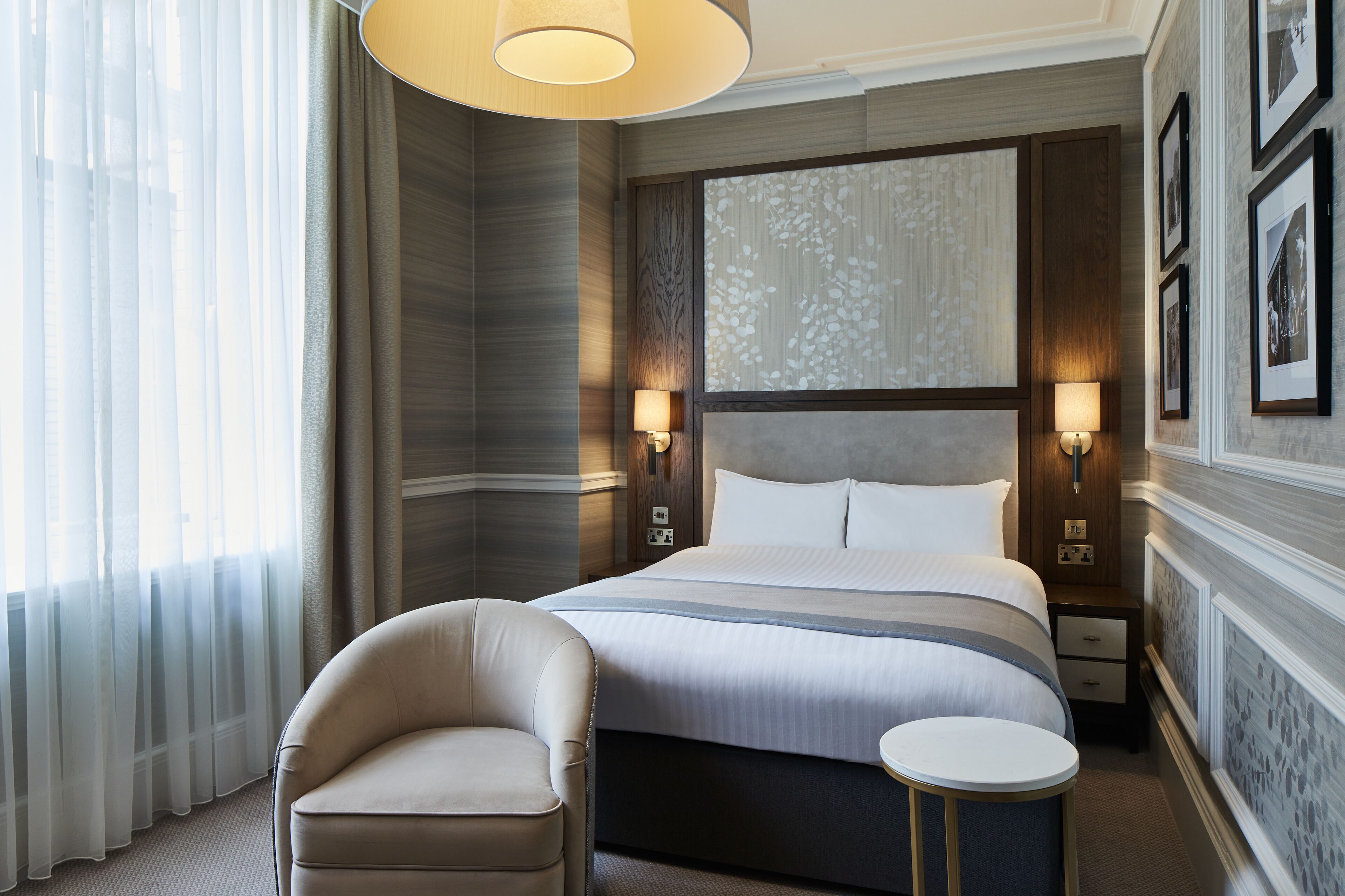 A hotel room with a large bed, two bedside tables, a chair, and a small side table.