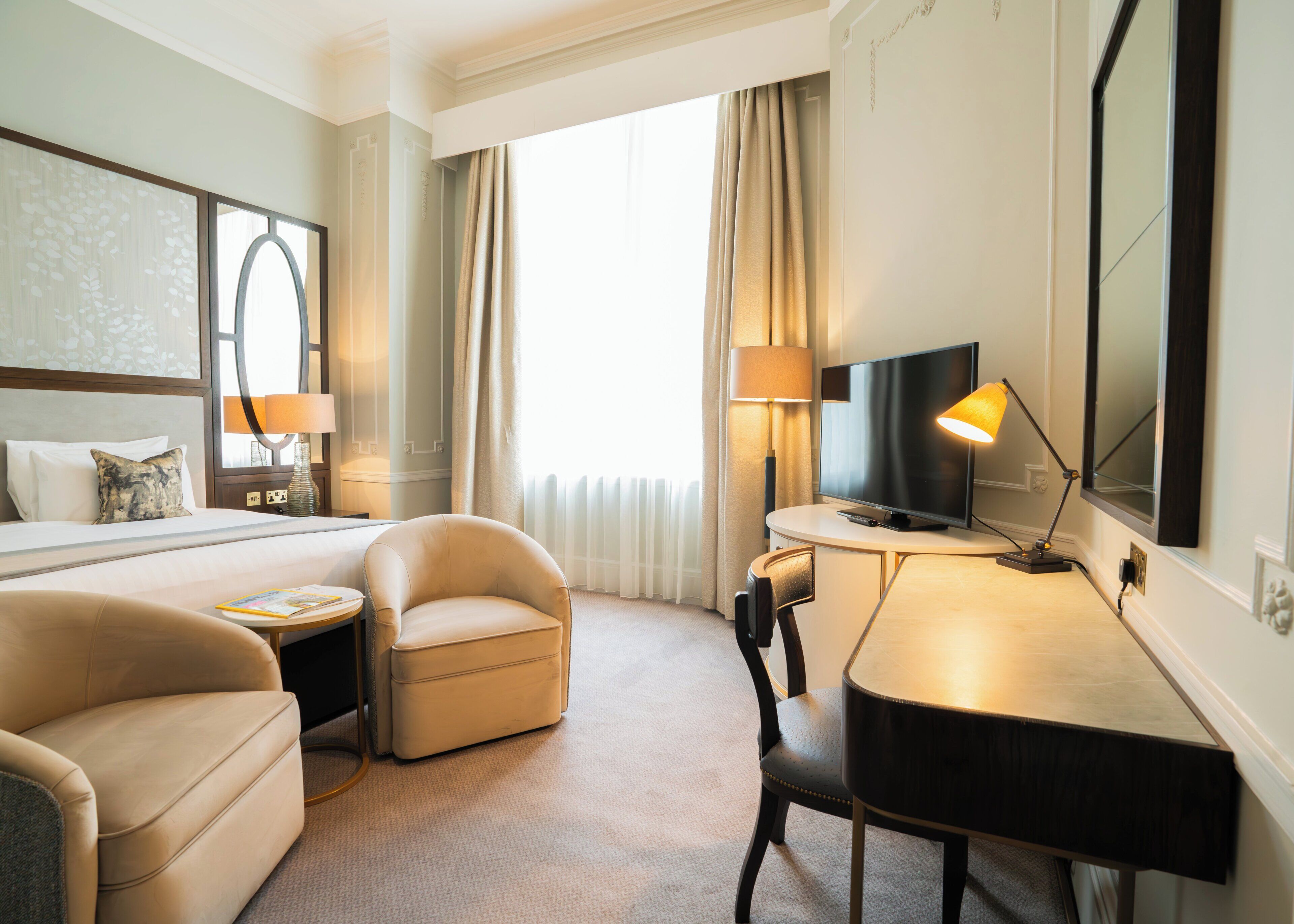 A hotel room with a bed, a desk, a chair, a television, and a lamp.