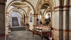 A grand hallway with marble floors, ornate columns, and a staircase leading to an upper level.