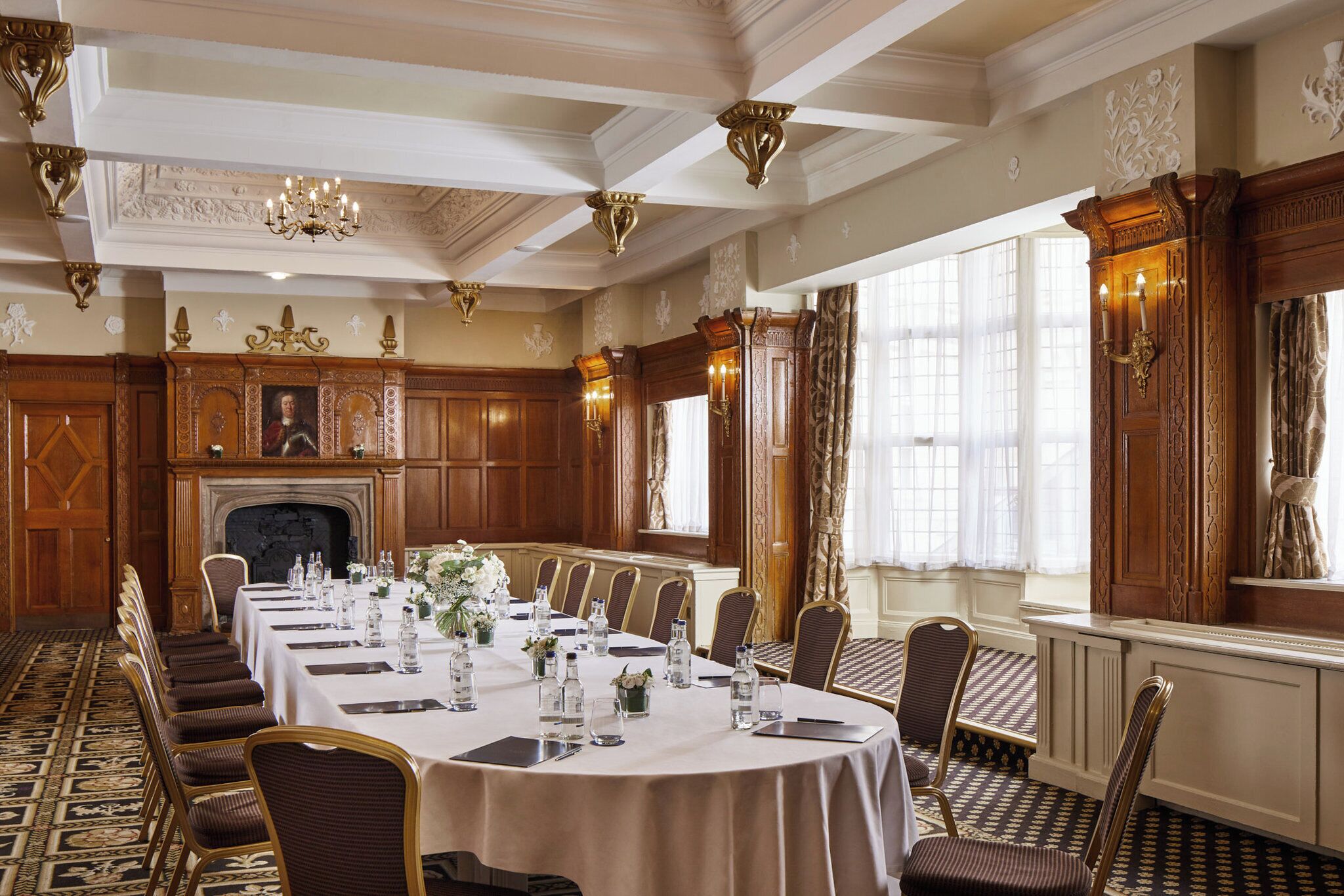 A formal dining room with a long table set for a banquet, ornate wood paneling, and a fireplace.