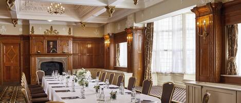 A formal dining room with a long table set for a banquet, ornate wood paneling, and a fireplace.